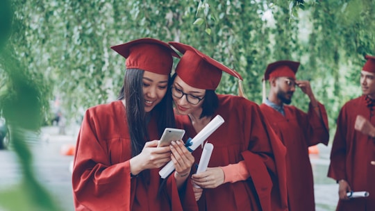 Two graduates in red gowns looking at a smartphone
