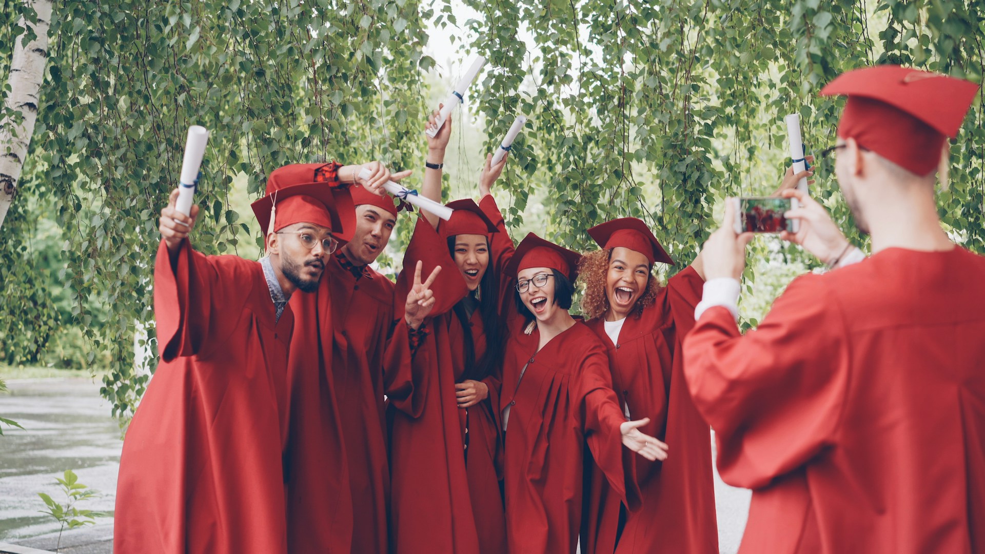 Graduates in red robes pose for a photo outdoors.