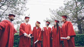 Graduates in red gowns holding diplomas outdoors
