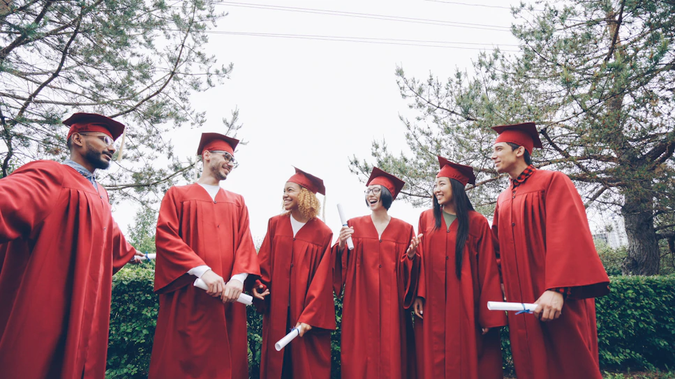 Graduates in red gowns holding diplomas outdoors
