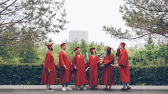 Graduates in red gowns stand together outdoors.