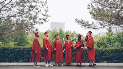 Graduates in red gowns stand together outdoors.