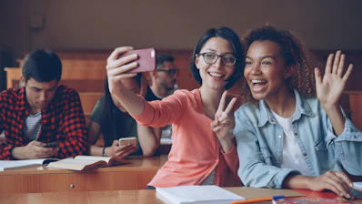 Two smiling students taking a selfie in a classroom.