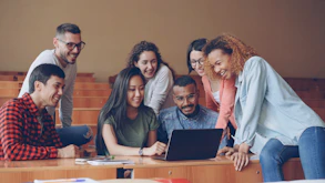 Diverse group of students gathered around a laptop.