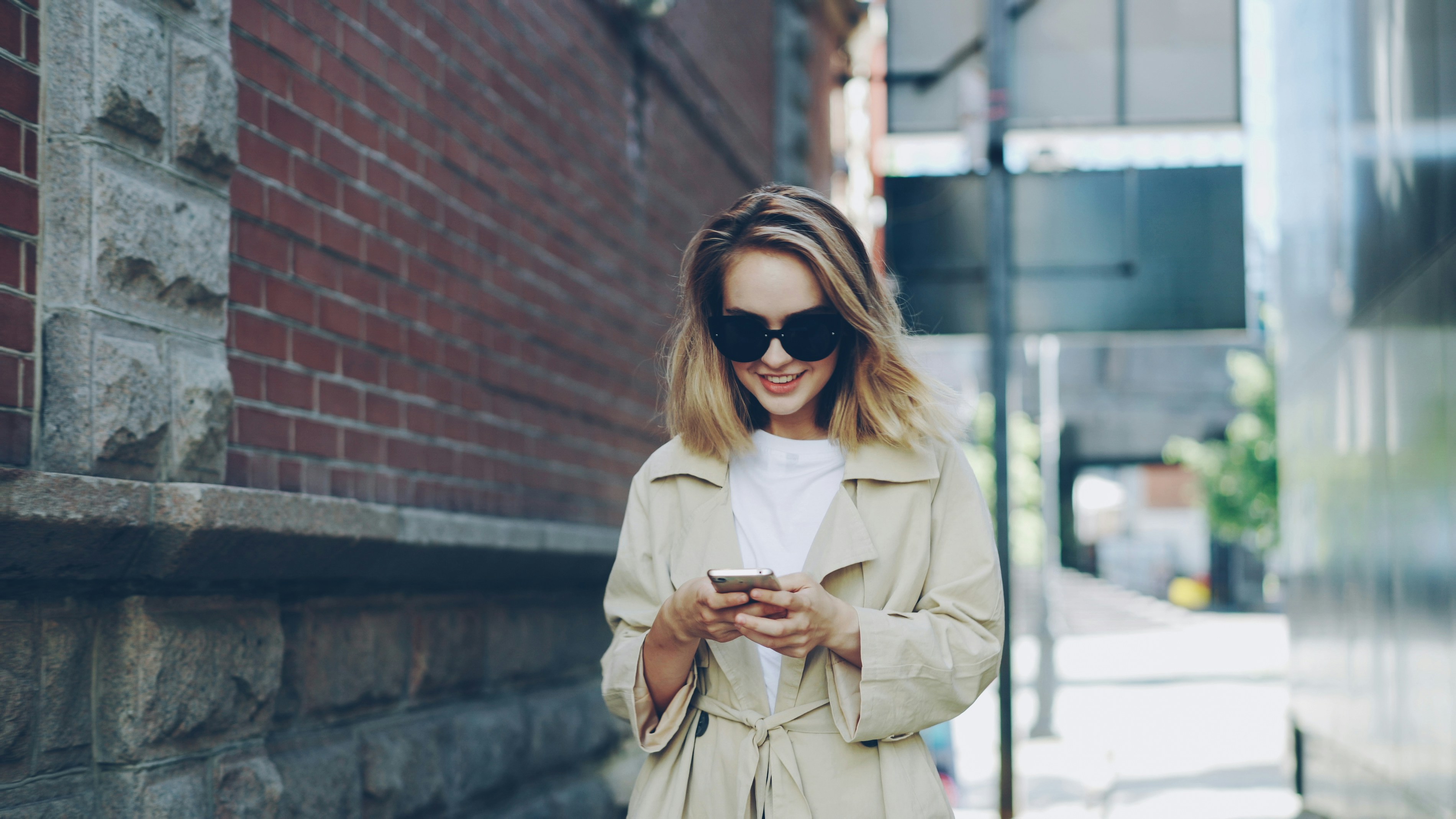 A smiling woman walks while looking at her phone.