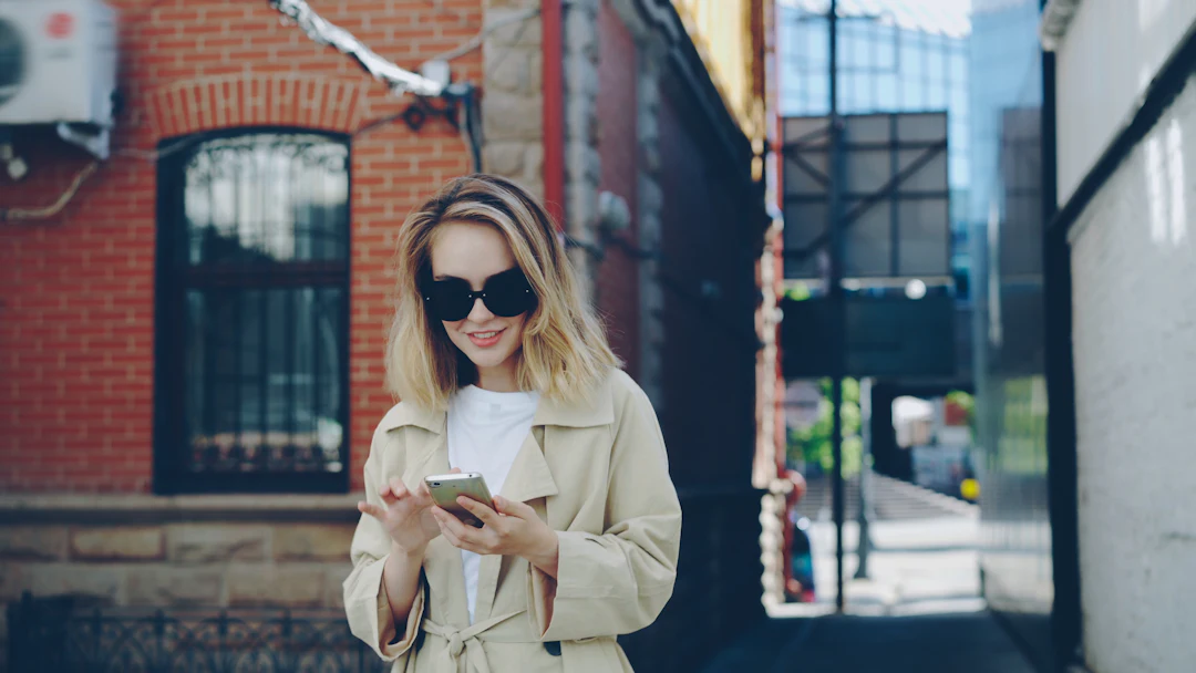 A creator in sunglasses checking her phone on a bright city street