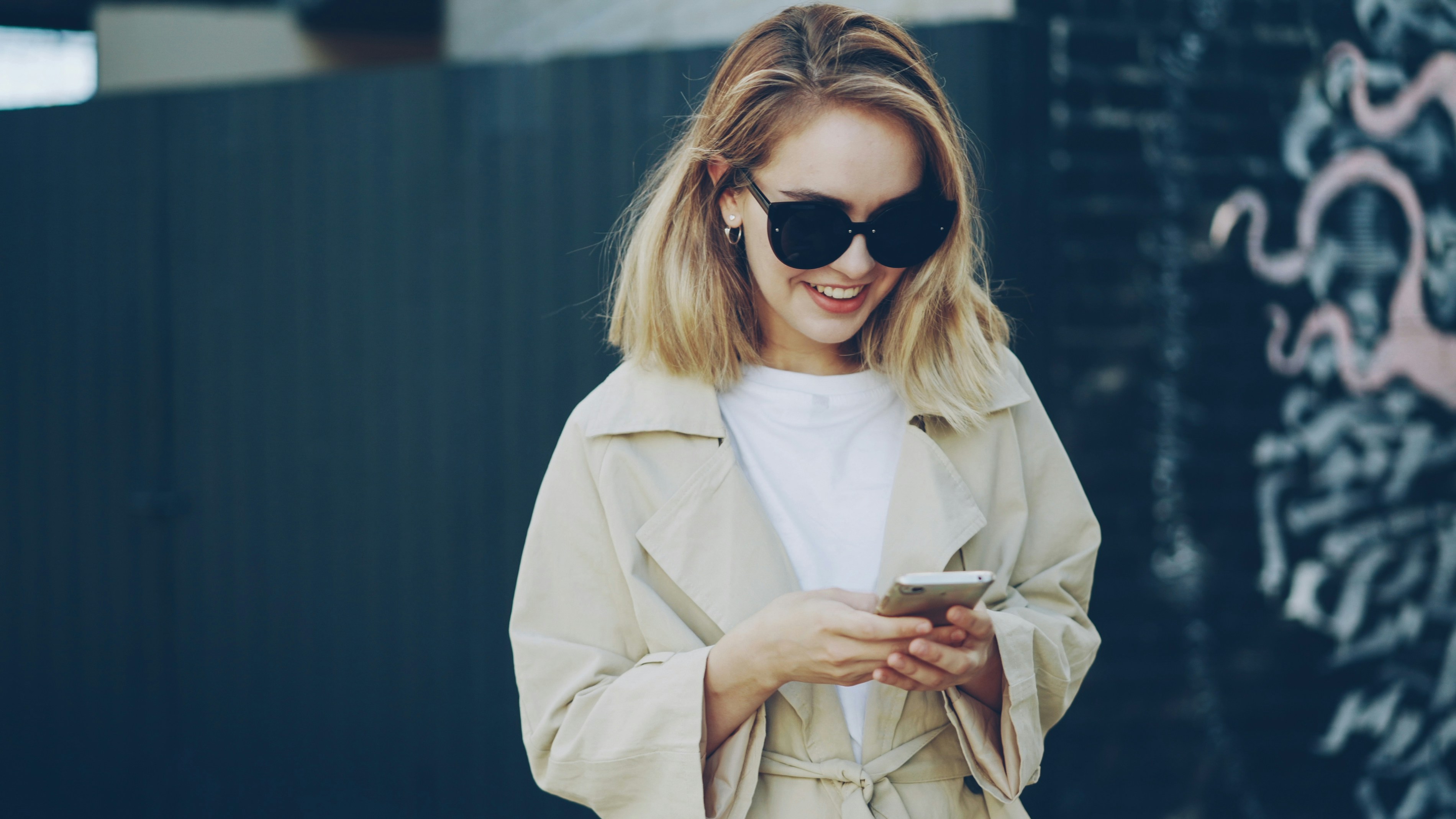 A young woman in sunglasses uses her smartphone.