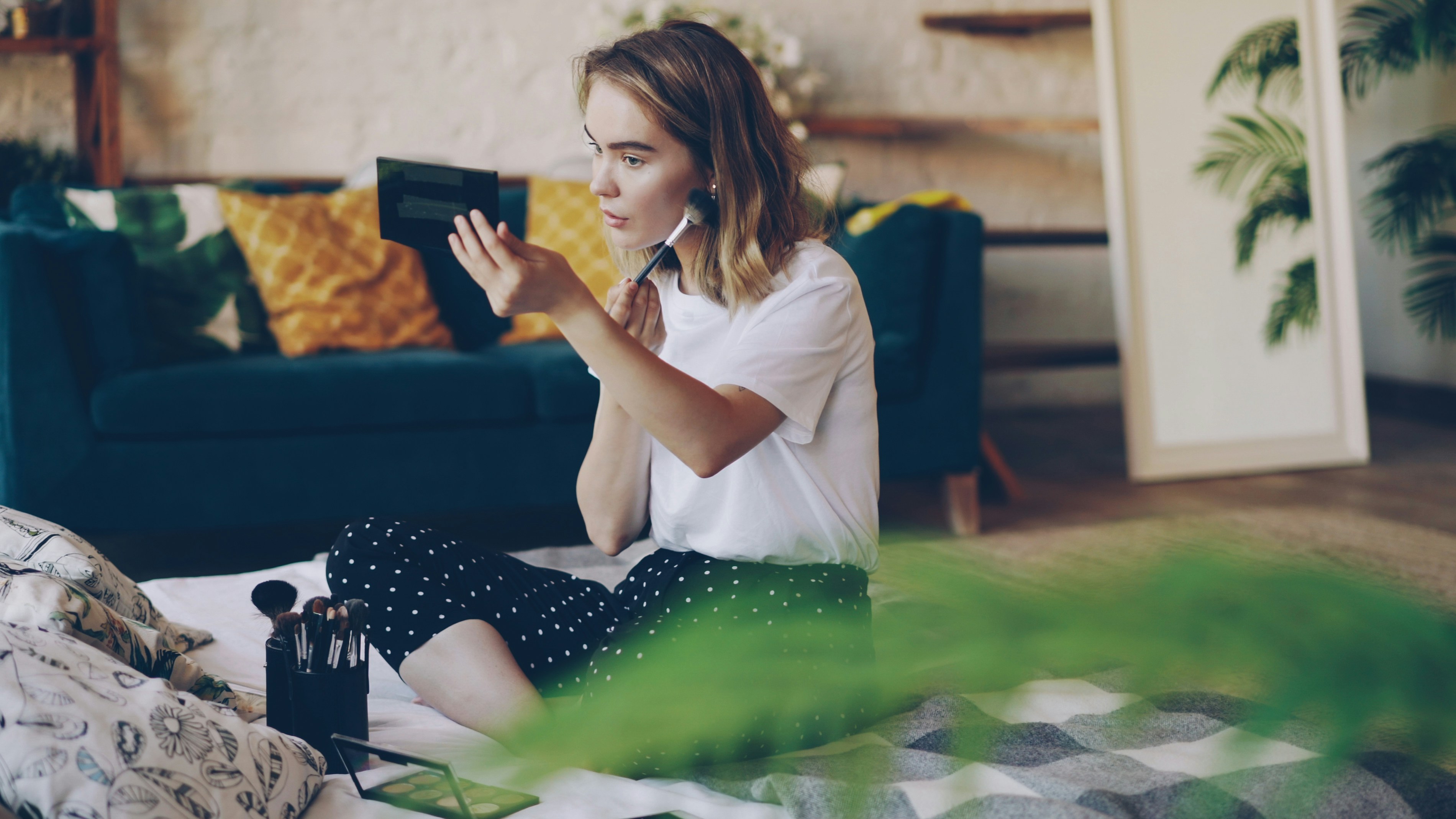 A young woman applying makeup in a bright room.