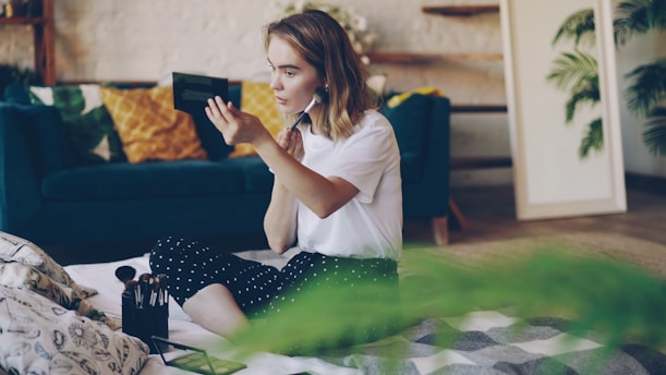 A young woman applying makeup in a bright room.