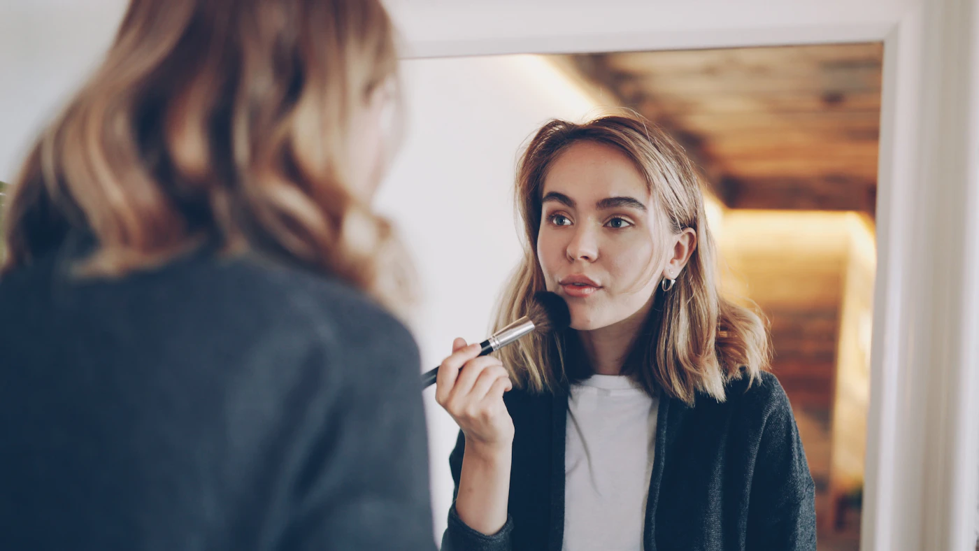 Woman applying makeup in front of a mirror