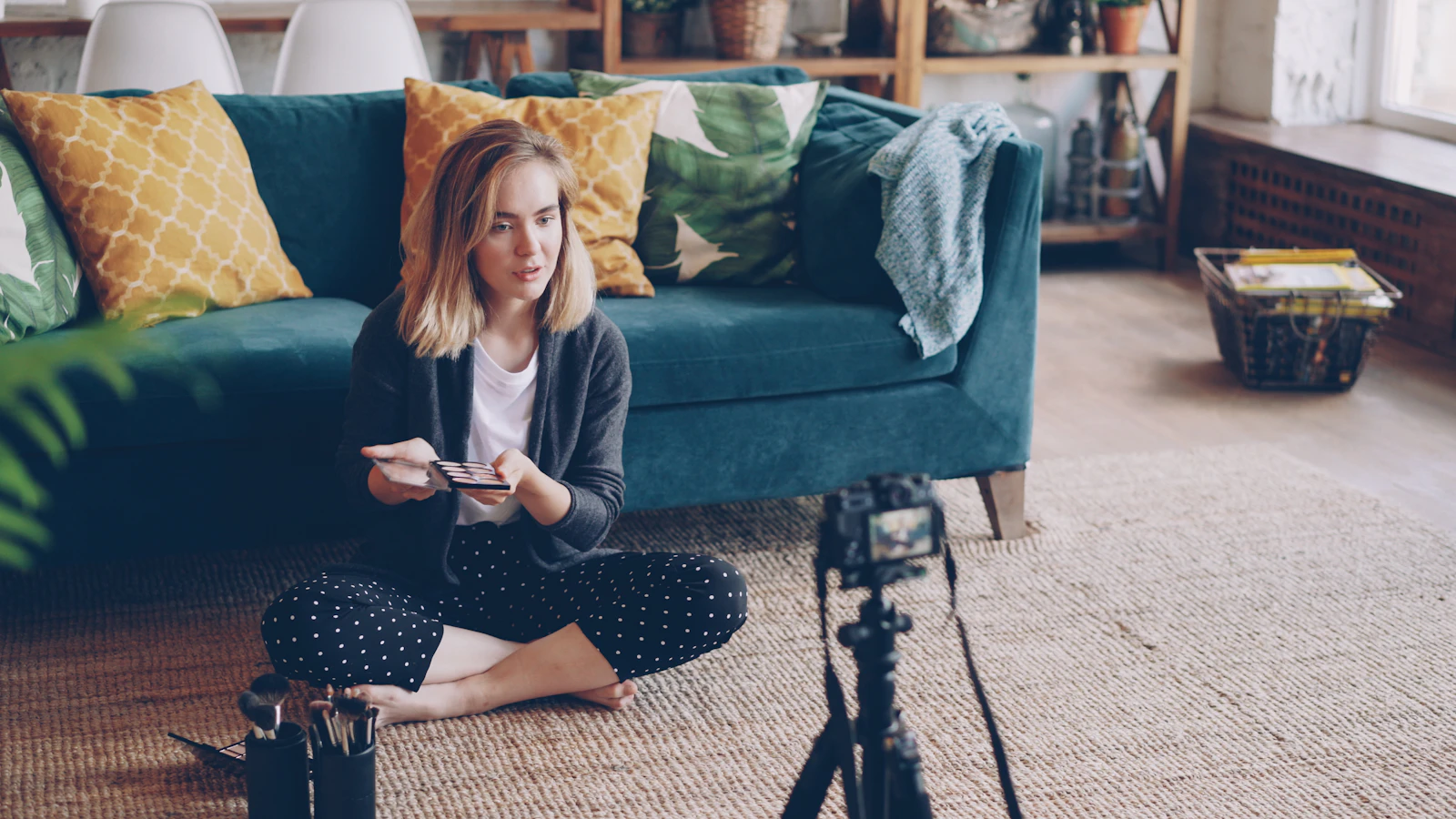 A creator sitting on a living room floor holding up a product while filming herself with a camera on a tripod