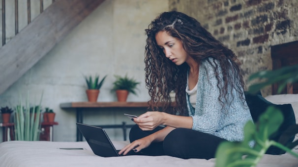 Woman using laptop and credit card on bed.