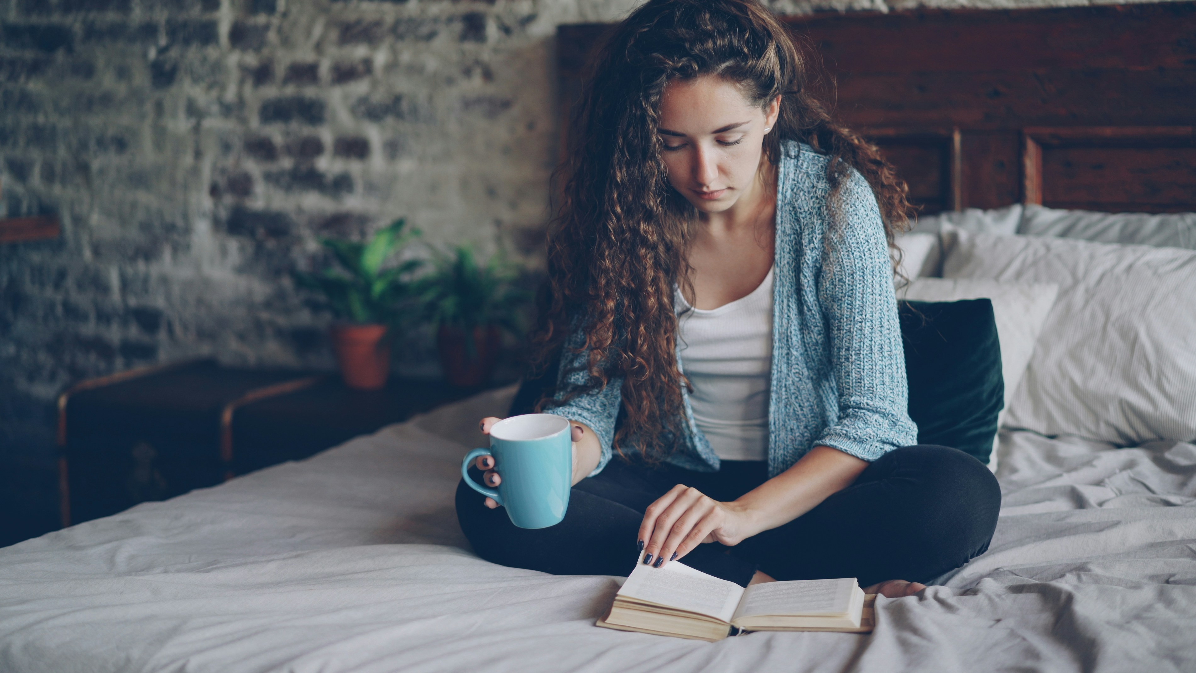 Woman reading a book and drinking coffee in bed.