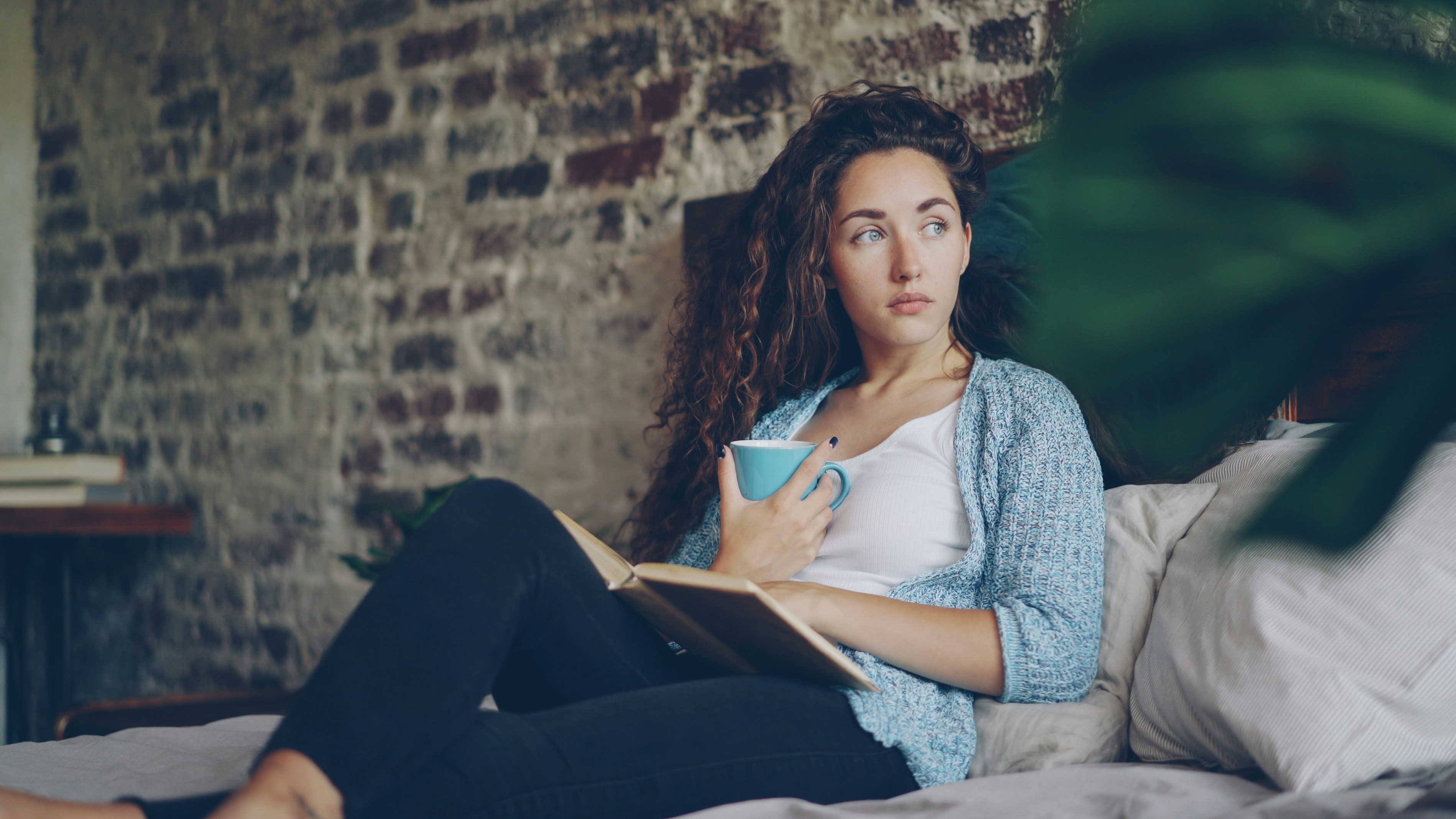 Woman holding coffee cup reading book on bed