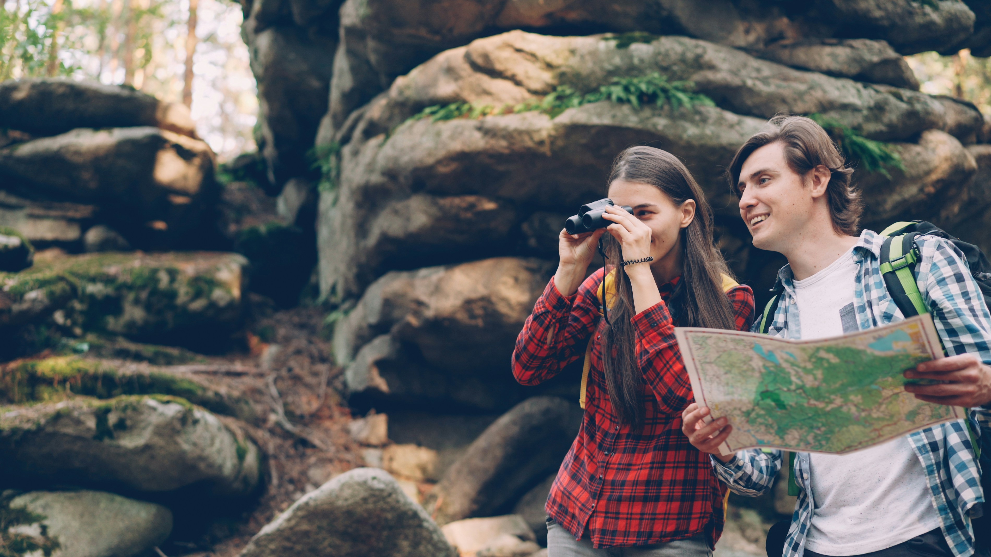 Couple hiking with map and binoculars in forest.
