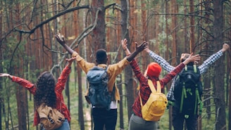 Four friends with backpacks raising arms in forest.