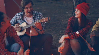 Friends laughing and playing guitar by campfire