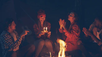 Friends celebrating a birthday around a campfire at night.