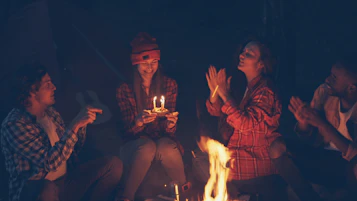 Friends celebrating a birthday around a campfire at night.