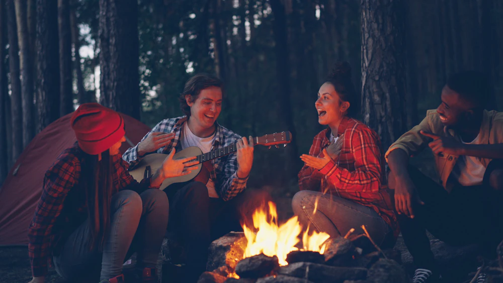 Amigos cantando alrededor de una fogata en el bosque