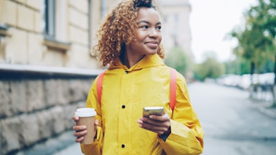 Young woman in yellow raincoat holding coffee and phone.