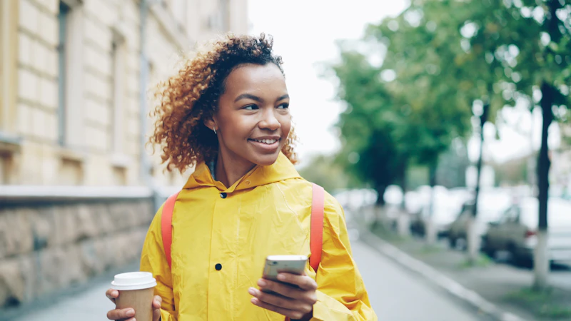 A woman holding coffee and checking her phone outdoors