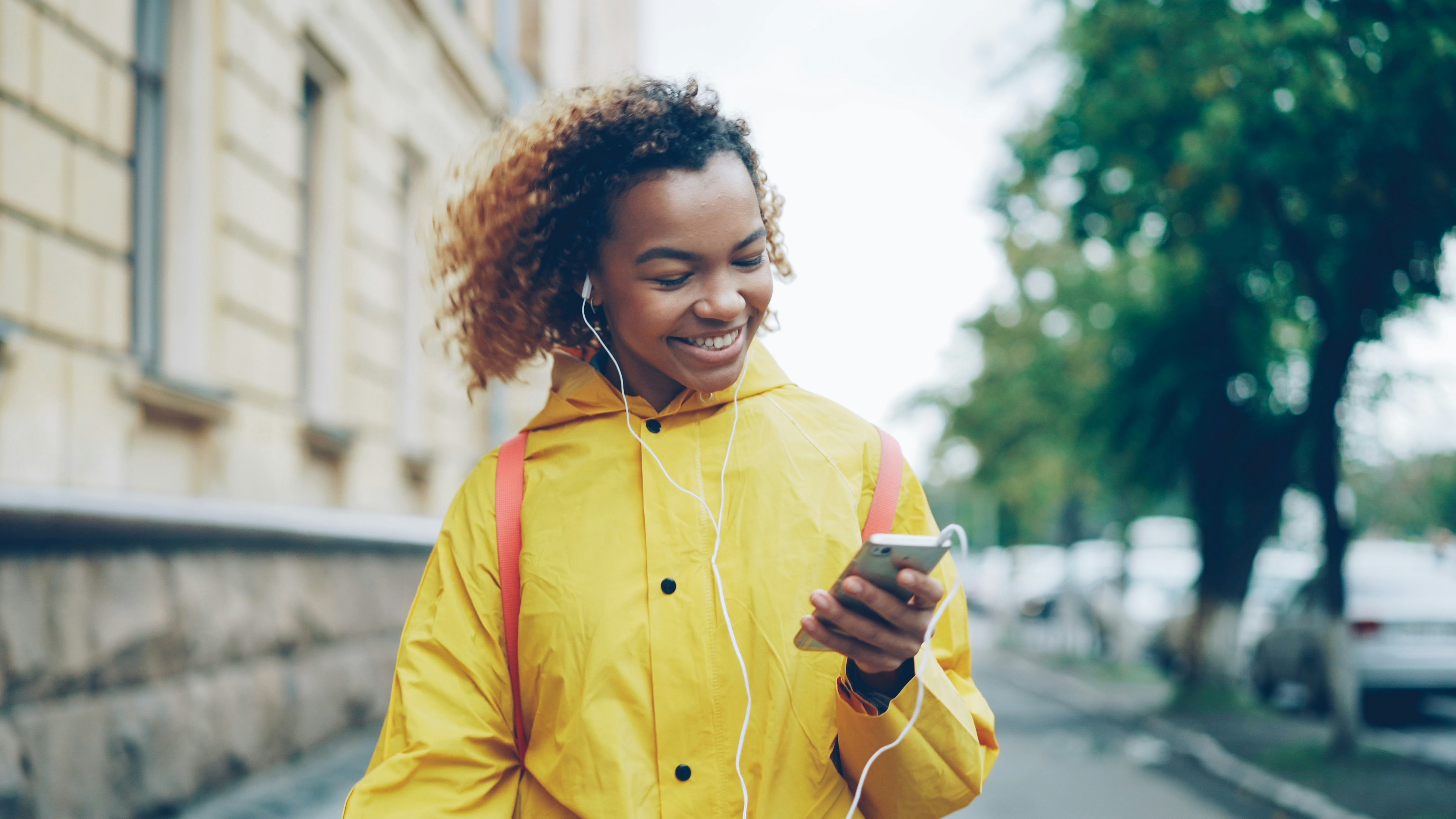 Young woman in yellow raincoat listening to music outdoors.