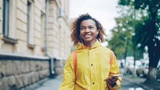 Young woman in yellow coat walks with headphones.