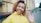 Young woman in yellow jacket waves hello outdoors
