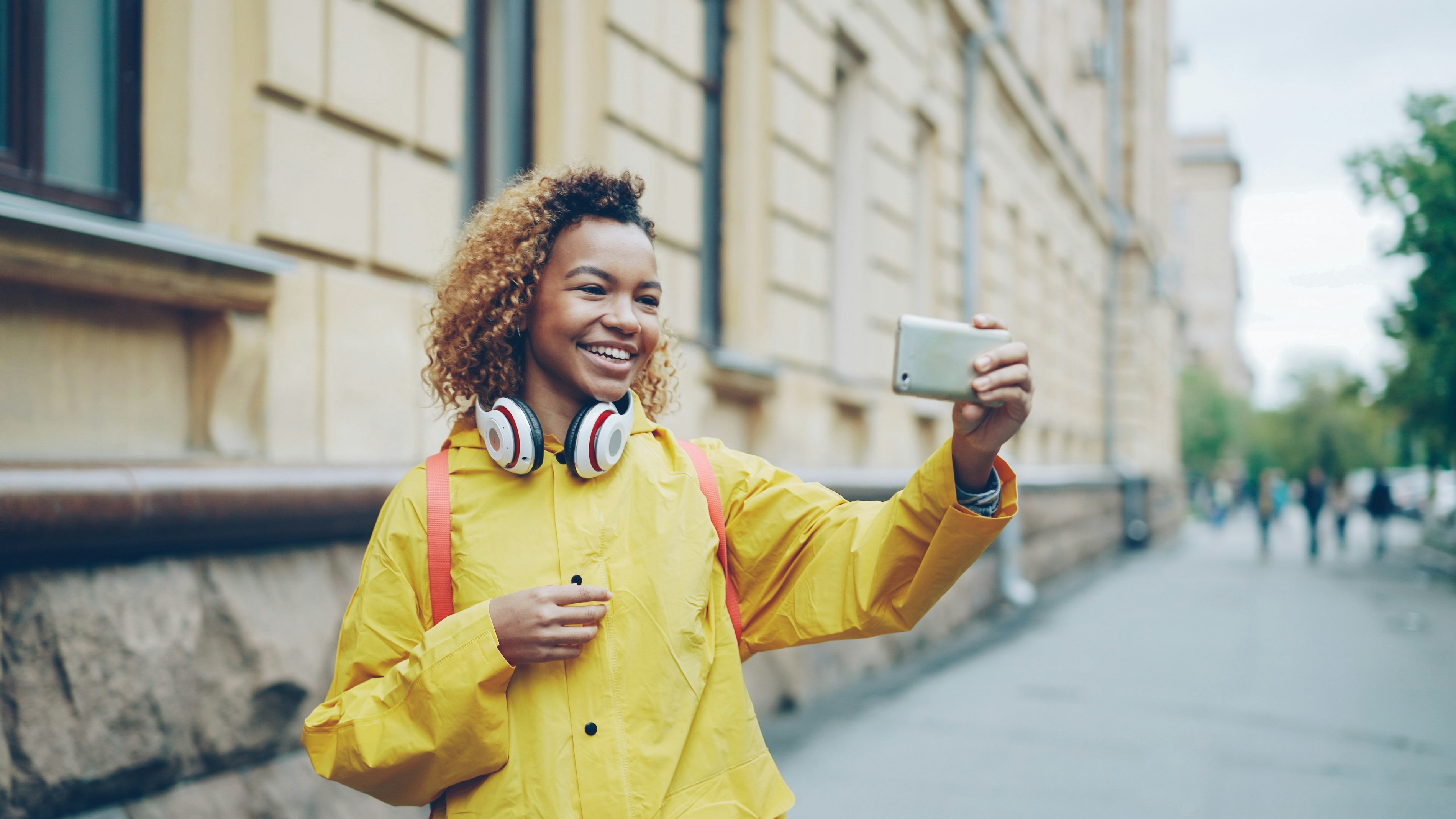 Young woman taking a selfie with her phone, Cheerful African American girl is making video call, speaking and laughing holding smartphone and looking at screen. Modern technology, joyful communication and young people concept.