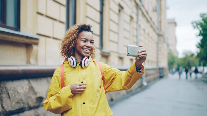 Smiling traveller in a yellow raincoat on a video call with her phone on a European street