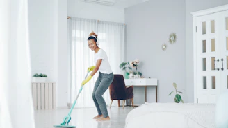 Woman happily mopping the floor in a bright room.