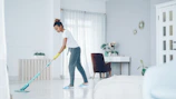 A woman mops a bright, modern living room floor.
