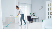 A woman mops a bright, modern living room floor.