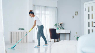A woman mops a bright, modern living room floor.
