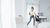 Woman with headphones cleaning and dancing happily