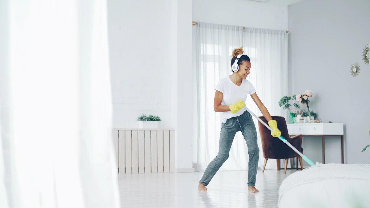 Woman with headphones cleaning and dancing happily