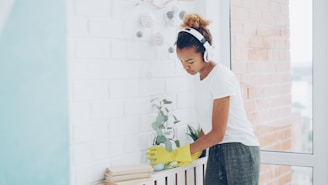 Woman wearing headphones cleans near a window.