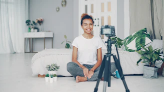 Young woman sitting on floor filming with camera.
