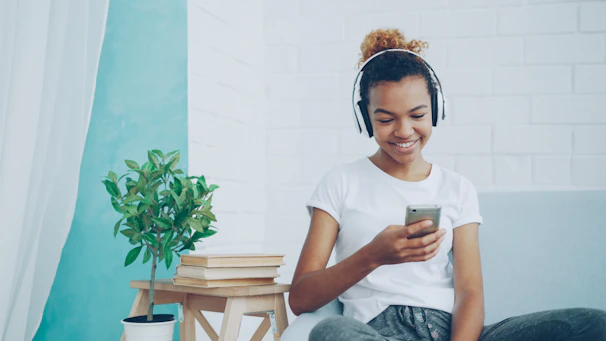 Young woman with headphones using smartphone on couch.