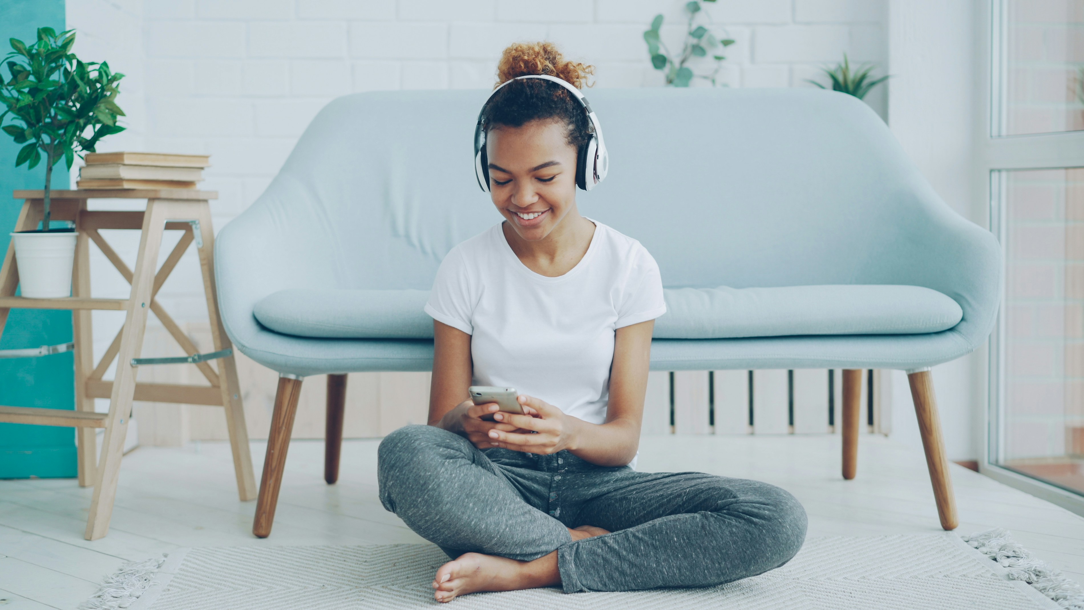Young woman with headphones using phone on floor