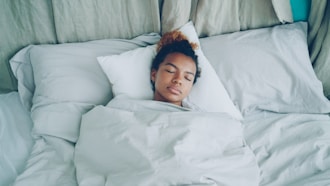 A young woman sleeping peacefully in a white bed.