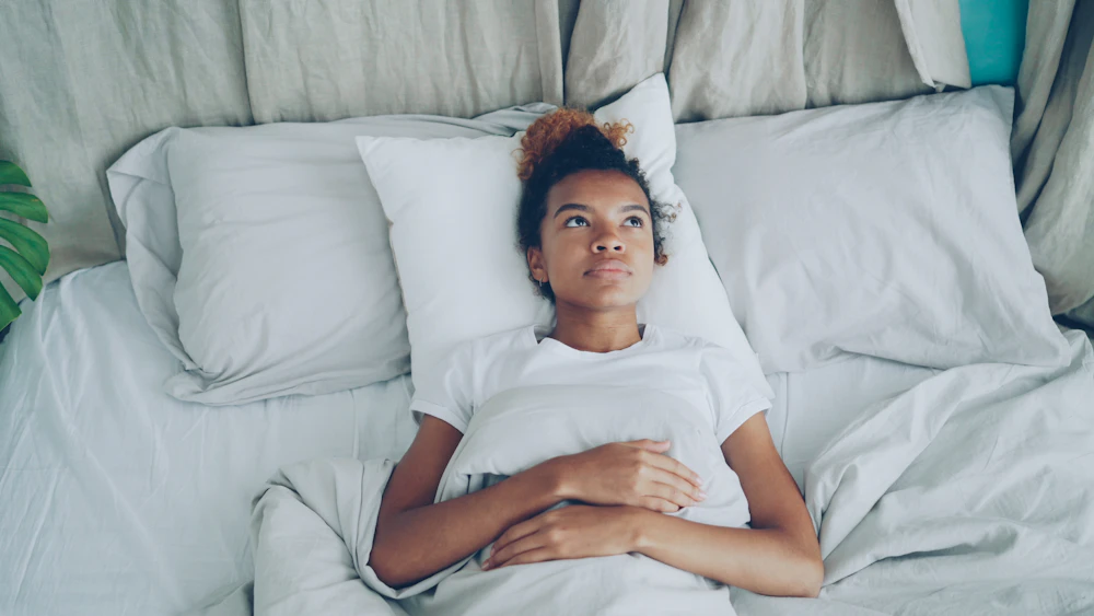 A young woman resting in bed with her arms folded over her stomach