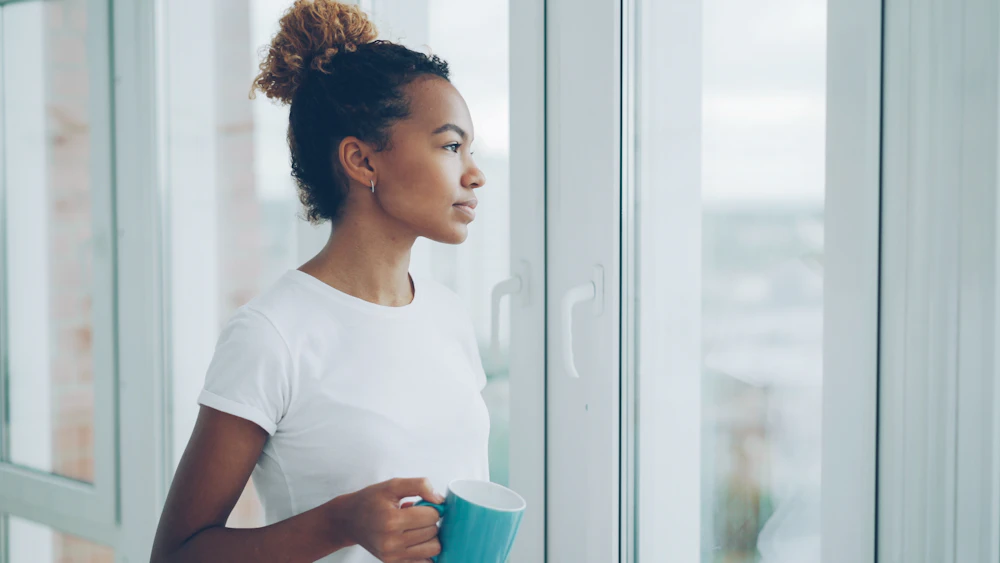 Woman looking out of a window with a mug, on a quiet weekday morning