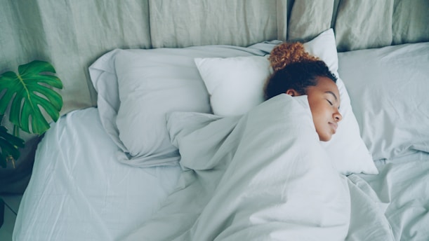 A young woman sleeping peacefully in a white bed.