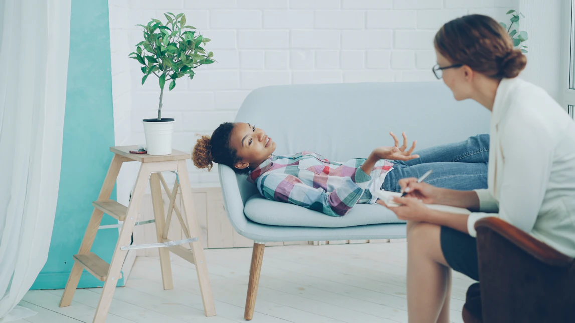 A young girl talks to a therapist on a couch.