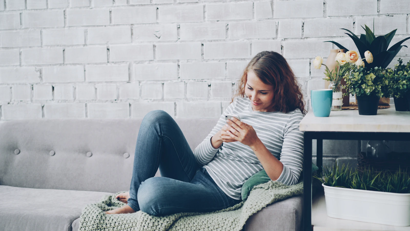 A young woman sitting alone on a sofa at home, using her smartphone.