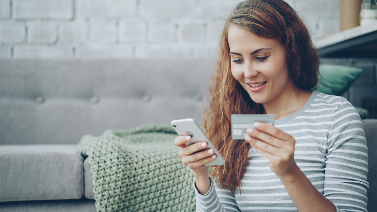 Mujer joven con una tarjeta bancaria en la mano haciendo un pago en línea desde su celular