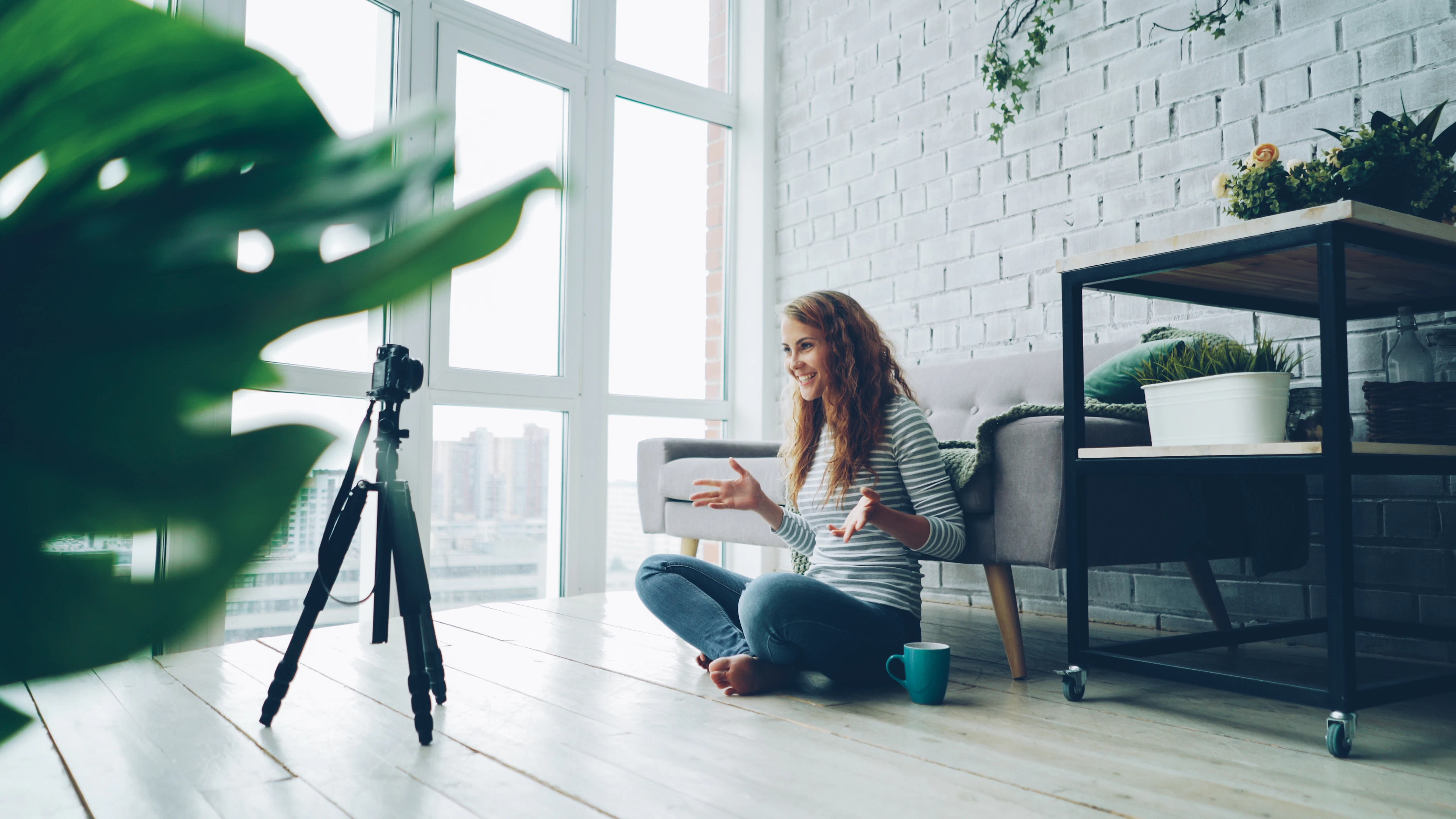 Woman filming herself with a phone in a bright white room beside a window