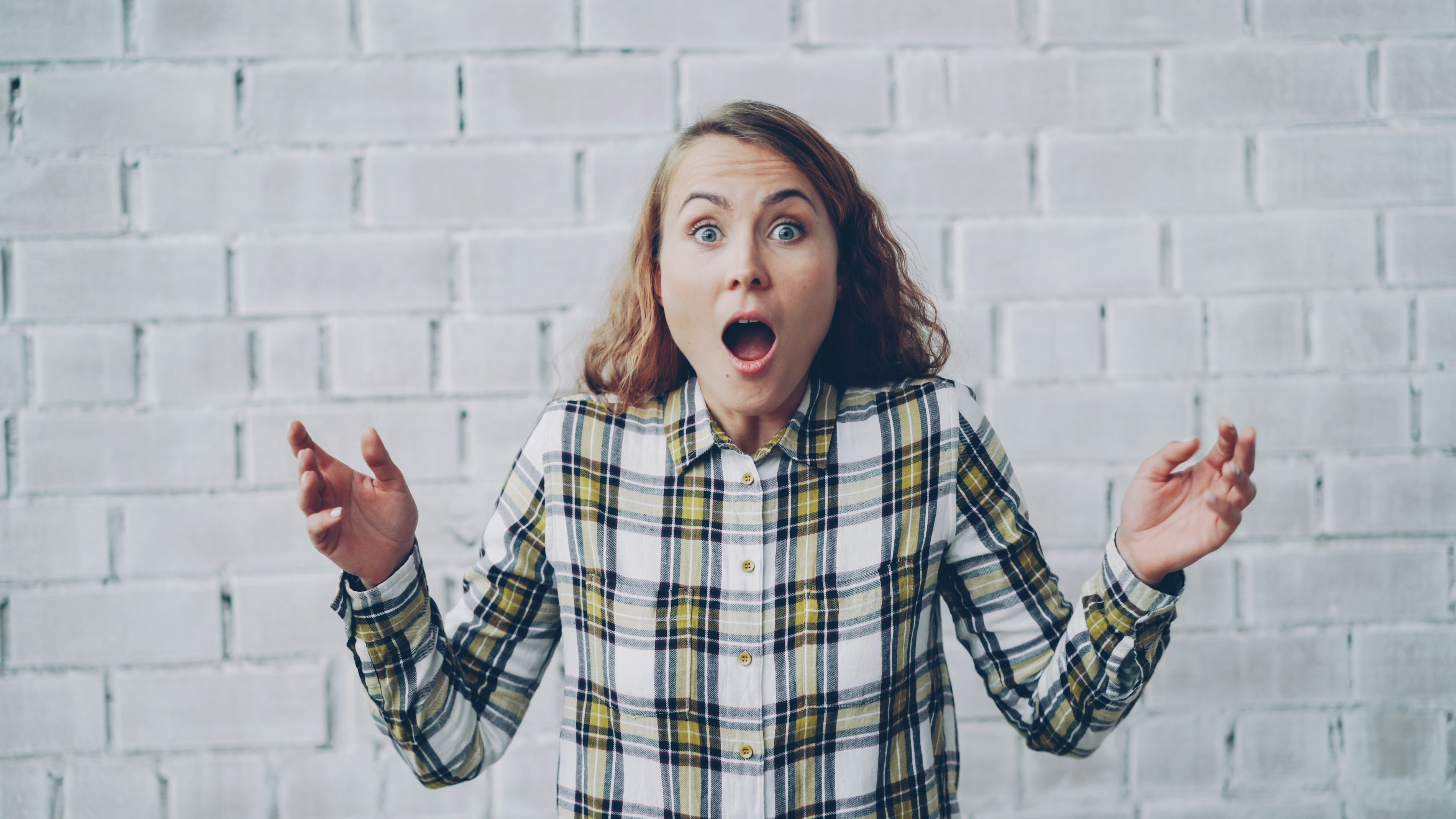 Young woman with surprised expression against brick wall